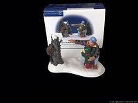 Front view of the figurine on top of its box showing two hikers and a tree stump on a snow base.