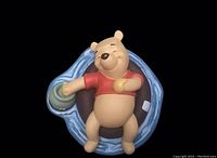 Top close-up view of Winnie the Pooh figurine lying on blue pool float, holding honey pot.