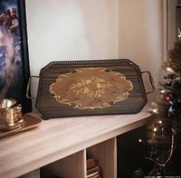 Satin wood vanity tray with floral marquetry inlay laid on wooden shelf beside decorative candle and Christmas tree.