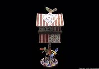 Front view of the enamel birdhouse stamp dispenser with a bird on top and insect figurines at the base.