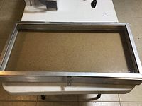 Rectangular metal frame with glass panel laying on a table, showing the whole item from above.