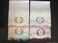 Four white embroidered towels laid flat showing floral embroidery in orange, pink, red, and blue colors, and crocheted edges in matching colors.