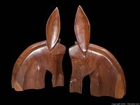 Pair of mid-century modern style wooden bookends carved in the shape of animal heads from a side angle showing smooth brown wood and pointed ears.