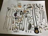 Overview of varied estate jewelry featuring chains, earrings, brooches, rings, pendants and bracelets arranged on white background.