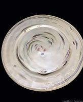 Top view of round iridescent white decorative glass plate with feather design and rippled texture.