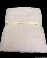 Folded pink linen twin duvet cover tied with a cream-colored ribbon on black background