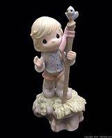 Front view of the Precious Moments figurine. Child stands holding a staff topped with a bird on a textured base.