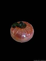 Front angled view of a small glass pumpkin with orange iridescent color and twisted green stem on top.
