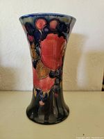 Front view of the Moorcroft vase showing the pomegranate pattern in red, black, and green on a dark blue base with a flared top.