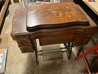 Full view of antique wooden sewing desk with cast iron legs and drawers, showing wear on the wood surface.