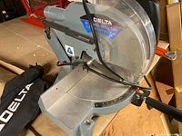 Full angle view of the Delta 10" power mitre saw showing base, blade guard, and dust collection bag.