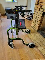 Overall view of green Handilite Walker positioned on wooden floor next to fireplace, showing padded arm supports and three wheels.