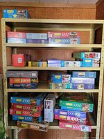 Photo of several shelves filled with assorted 1000-piece jigsaw puzzle boxes of mostly Milton Bradley brand with visible scenic and village artwork.