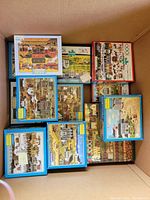 Overall view of all puzzles in box, showing mostly Charles Wysocki puzzle titles in blue and white boxes, plus one puzzle with a red border.