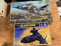 View of the two vintage model airplane kits: AV-8A Harrier and Lockheed SR-71 Black Bird with colorful box art on wood surface.