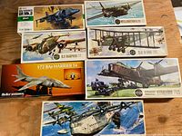 Photo showing seven vintage model airplane kits with colorful box art depicting Harrier, Wellington, Short Stirling, and RAF R.E.8 aircraft. Boxes are unopened and arranged on wooden surface.