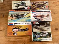 Lot includes vintage aircraft model kits arranged on wood surface with box art visible, featuring Hawker Hurricane, Fairey Battle, British Spitfire, Sopwith Camel, DHC Beaver, Fairey Firefly 5, and HS Harrier GR3.