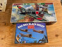 Top-down view showing both vintage model airplane kits with colorful box art of Japanese WWII planes, including model 52 and Baa Baa Black Sheep Japanese Zero.