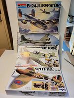 Three unopened vintage aircraft model kits on table, including Monogram B-24J Liberator, MPC Messerschmitt Bf 109E, and MPC Supermarine Spitfire Mk.1a, showing front packaging art.