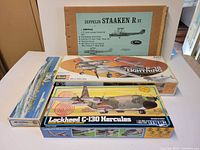 Four vintage model airplane kits boxed and partially stacked showing brand logos and labels of P-38 Lightning, Lockheed C-130 Hercules, and Zeppelin Staaken R.VI