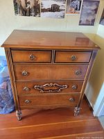 Front view of vintage wooden chest of drawers showing five drawers and decorative elements