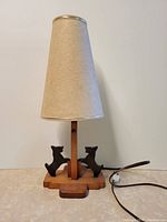 Front view of the vintage lamp showing wooden base with two dog carvings and beige fabric shade.