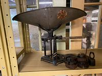 Full view of vintage cast iron balance scale with large weighing dish on top, sliding measurement arm, black finish with wear, and the assorted cast iron weights on the side.
