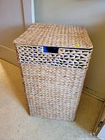 Full view of rectangular woven laundry hamper closed with lid in place.