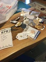 Overview of religious pins and pendants including angels, crosses, and saints scattered loosely on a wooden surface, with some items still tagged and bagged.