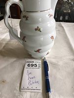 Photo showing the full pitcher to detail the bee hive shape and floral design, with a pen and lot card for scale.
