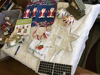 Overview photo showing red felt Santa stocking, glass pumpkin ornament, clear star tree topper, small framed artwork, and several small Christmas figurines and ornaments on white surface.