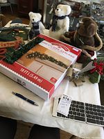 Three Boyds Bears plush toys and boxed 18-foot pre-lit pine garland on a table with some small Christmas decorations