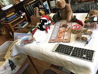 Wide view of Christmas Boyds Bears figurines, wooden snowman Welcome sign, plush skunk, and small holiday boxed items on table.