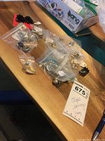 Various clip earrings and one black jagged ring on a table. Earrings mostly in individual plastic bags with tags. Seller's note card showing lot number and description.