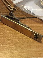 Close-up of a gold-tone tie bar with a triangular club crest emblem on one end, showing polished surface and clip back.