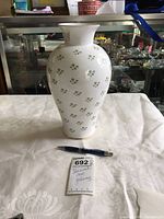 Front view of white ceramic vase with shamrock pattern and gold accents on table with pen and note card.