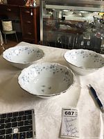 Set of three white porcelain serving bowls with blue floral garland pattern and silver rim on a white tablecloth, alongside a pen and keyboard for scale.