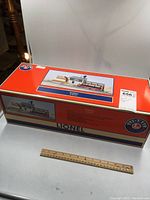 Full view of the Lionel sawmill sealed in original box with ruler for size reference.