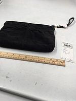 Black suede clutch purse folded flat on white surface, with measuring ruler showing approximately 9 inches in width.