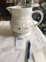 Full view of ceramic pitcher on table alongside a blue pen for size reference and the lot tag