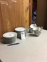 Photo showing stacks of small plates, saucers, and several stacked teacups on a table against wood paneling.