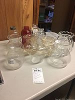 Collection of short and squat shaped glass lamp globes on white table, showing variety of clear and red colored glass globes.