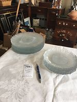 Clear view of stacked clear glass plates pressed with sunflower patterns, showing smaller salad plates and larger dinner plates separately stacked on a white tablecloth.