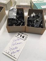 Close-up of two open boxes containing black metal model train truck assemblies and parts with handwritten lot tag