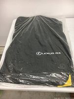 Top view of black vehicle mat with 'Lexus RX' logo visible through plastic wrapping, showing condition and packaging.