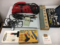 Photo shows a collection of handyman tools including a Dirt Devil vacuum, two soldering irons with stands and manuals, a boxed Super 10 DIY tool kit, a boxed Shopmate tool, and a blue tool case with sockets and ratchets.