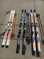 All three sets of downhill skis with matching poles laid out side by side on concrete.