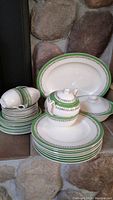 Stack of dinner plates, cups, and serving platter with green decorative patterns and floral accents on white china.