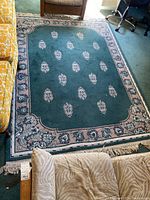 Full view of the rectangular area rug with green field and floral medallion patterns.