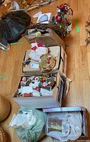 Photo shows multiple boxes and bags containing assorted Christmas ornaments, brown paper packaging, and large lamp in background.